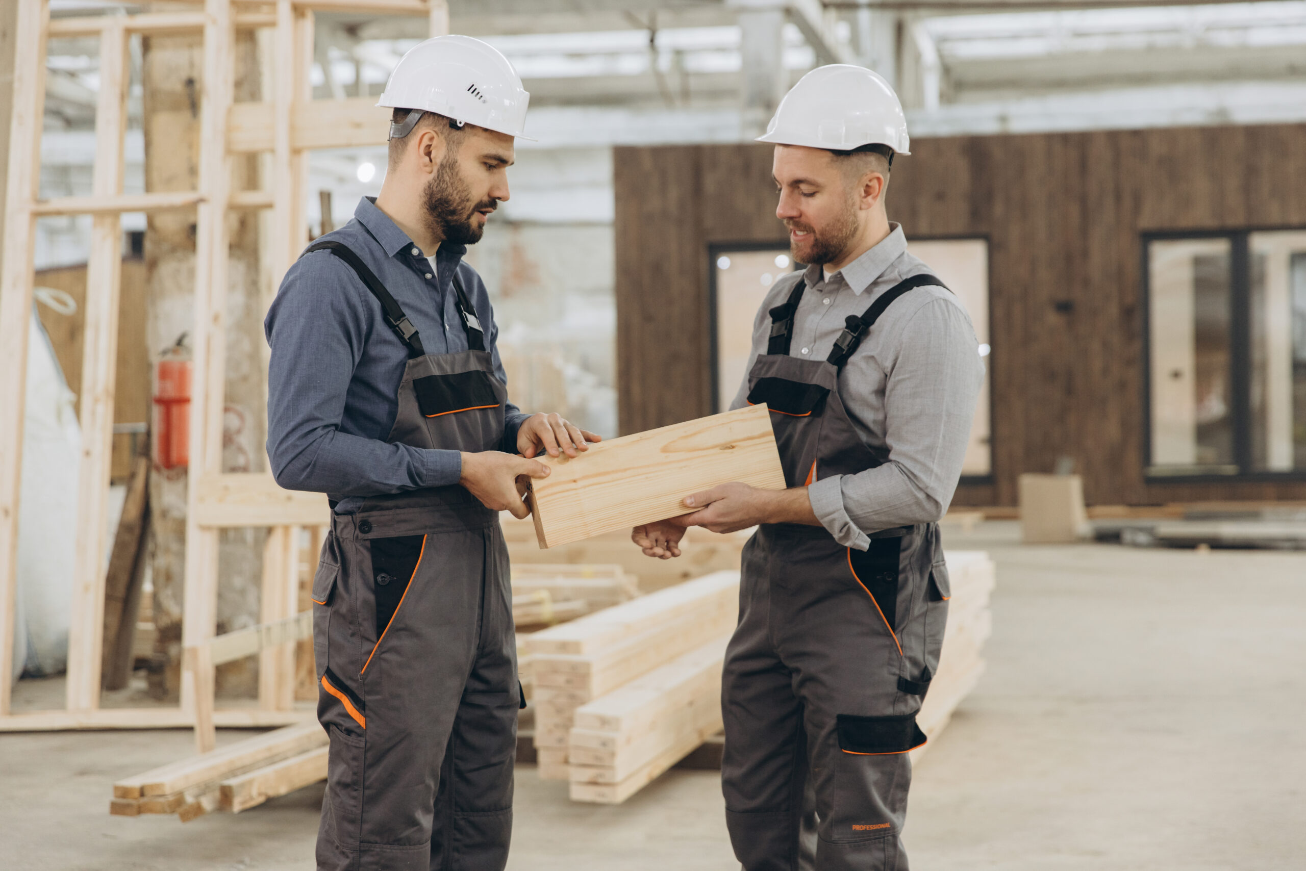 Dwóch pracowników Fabra w odzieży roboczej i kaskach ocenia kawałek drewna w hali produkcyjnej