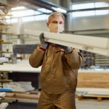 Pracownik przenosi drewniany element w hali produkcyjnej