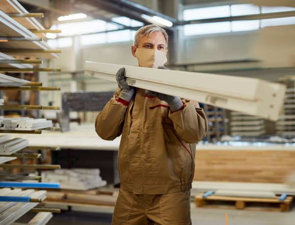 Pracownik niesie drewniany element przez halę produkcyjną